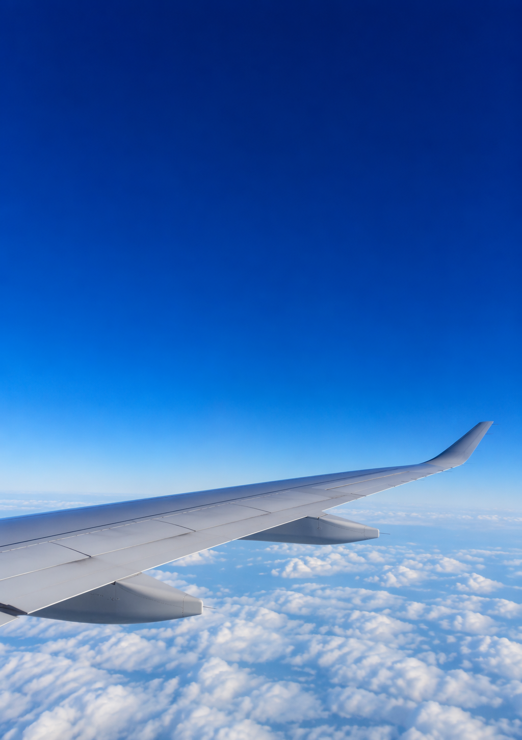 Airplane wing above a layer of white clouds in deep blue sky