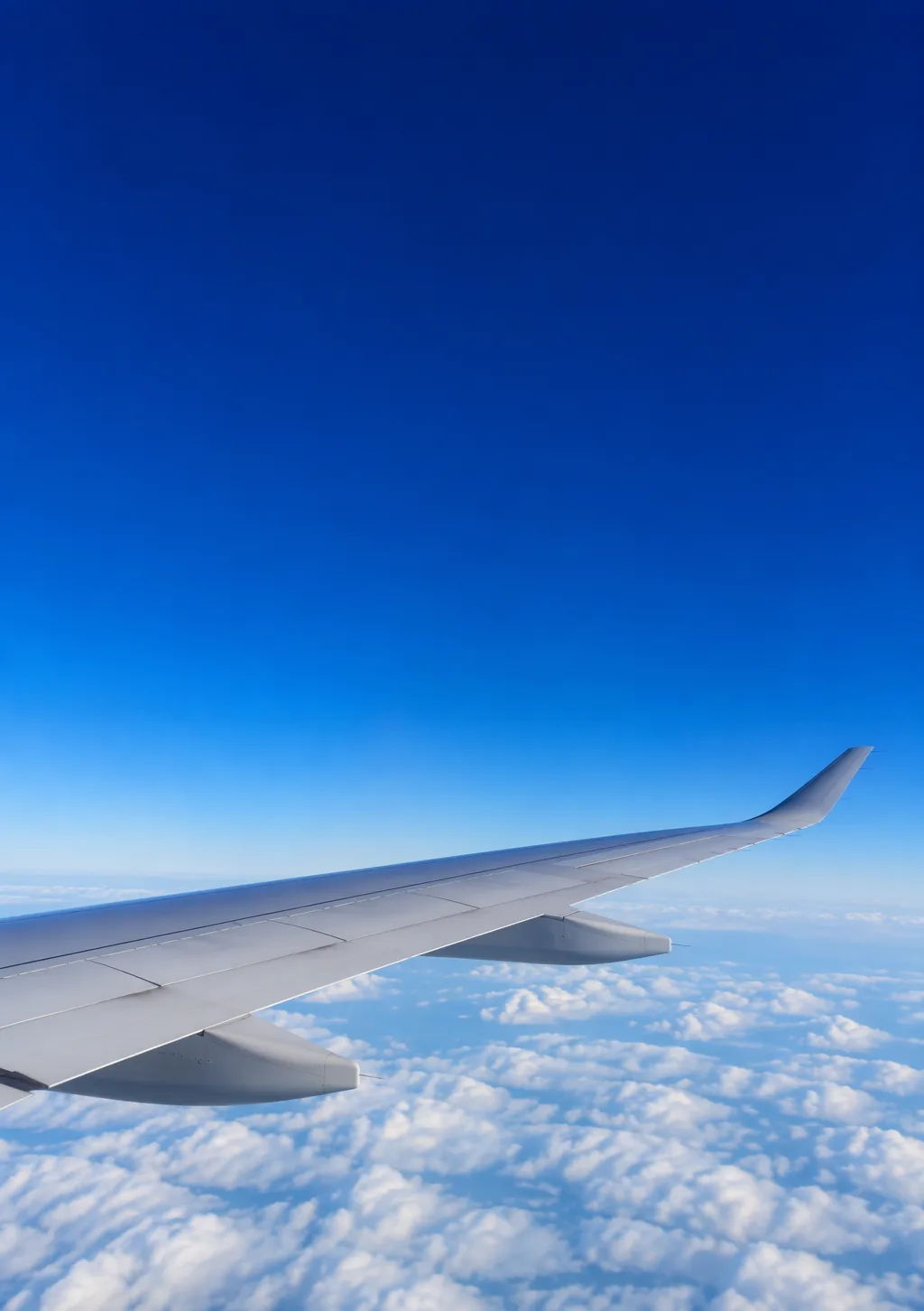 Airplane wing above a layer of white clouds in deep blue sky